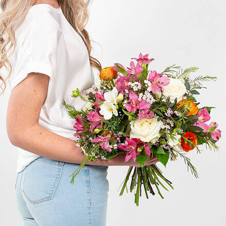 Eine Frau hält einen weiß, pink, orangenen Blumenstrauß in der Hand.