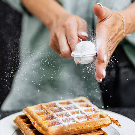 Person bestreut Waffel mit Puderzucker