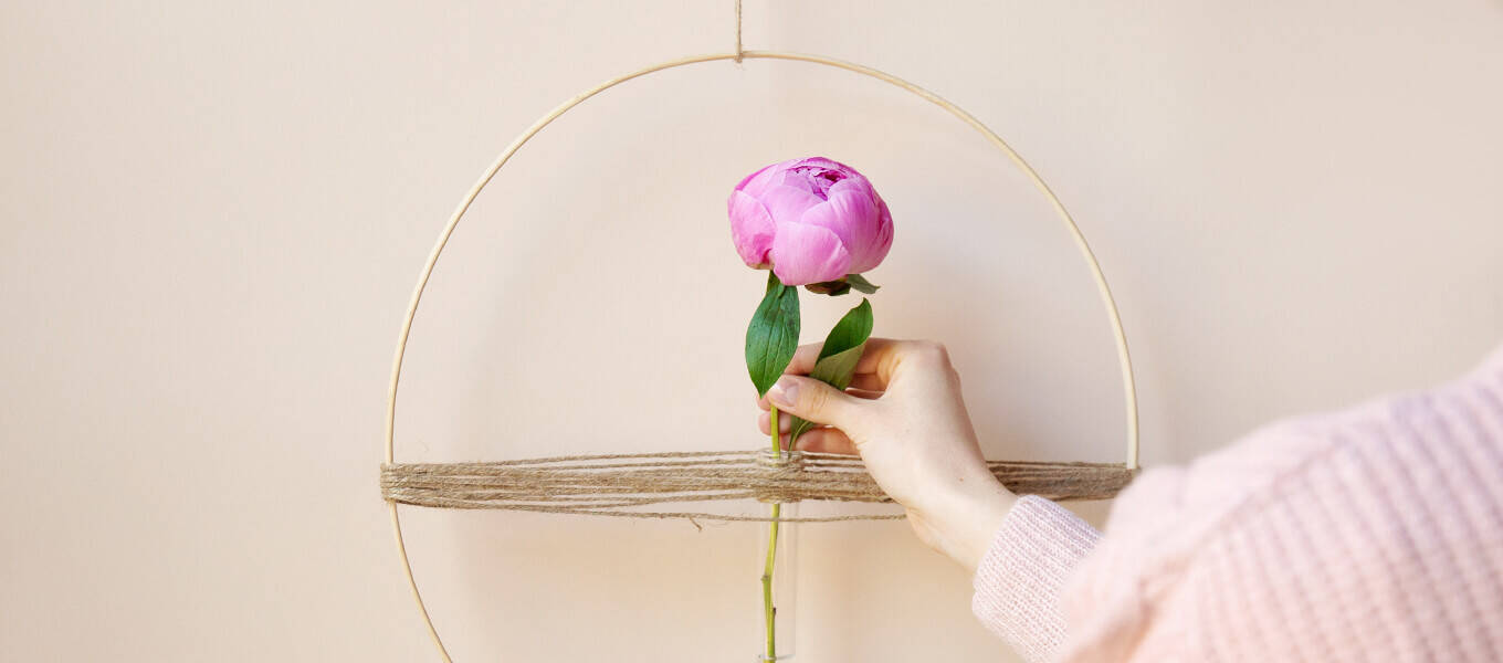 Frau steckt eine Pfingstrose in einen DIY-Blumenring mit Reagenzglas