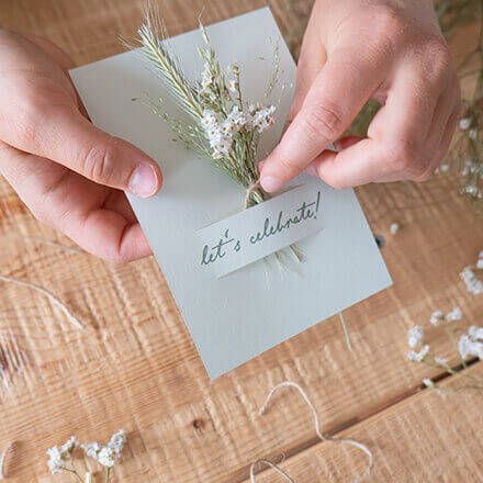 Ein Mini-Trockenblumenstrauß wird durch einen Schlitz in einer Hochzeitseinladungskarte gesteckt