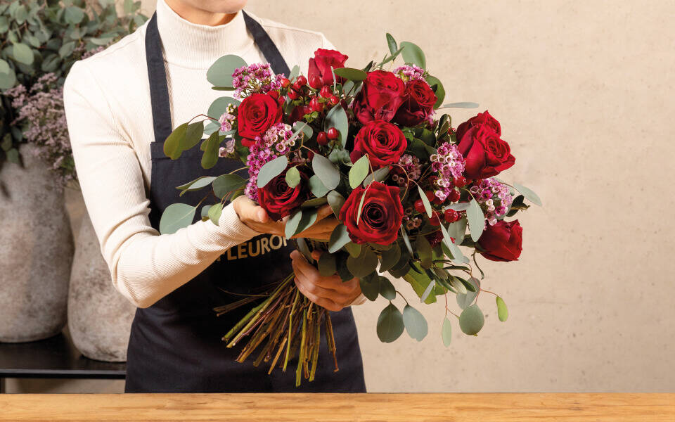 Eine Floristen hält einen großen Strauß rote Rosen in die Kamera.