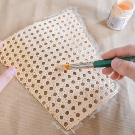 Wiener Geflecht wird auf einer Pappunterlage mit Hilfe eines Pinsels und Acrylfarbe in einem zarten Rosé-Beige bemalt.