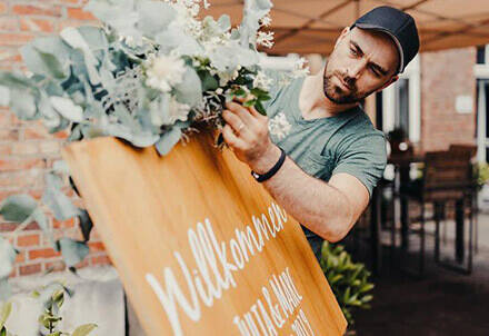 Florist, der ein Willkommensschild mit Blumendeko herrichtet