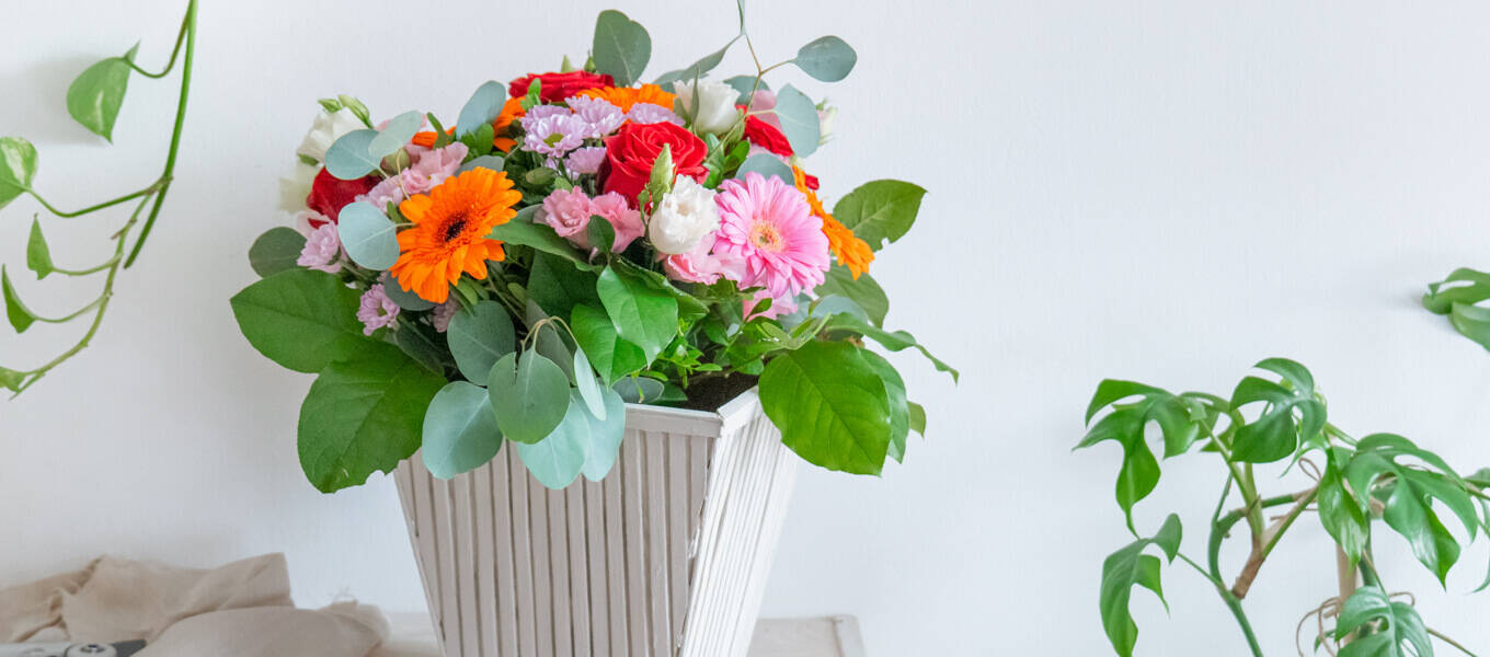 Upcycling-Idee einer Flower-Bag zu einer Vase mit Bambusstäben, die senkrecht an der Flower-Bag angebracht worden sind und danach farblich mit Kreidefarbe in Taupe gestaltet wurde.