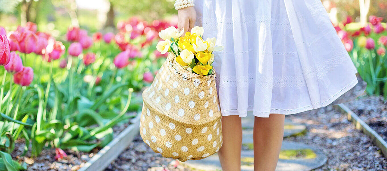 Ein Garten im Frühling. Eine Frau steht mit einem Korb, mit Tulpen drinnen im Garten.