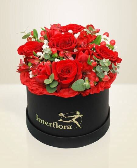 rote Rosen, Blumenarrangement, runde Geschenkbox, grünes Laub, Blumen-Geschenk, rote Rosen, Blumenstrauß, runde Hut-Box, Grünblätter, Interflora-Logo auf Schachtel