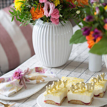 Zu sehen ist eine gedeckte Tischecke, welche mit Blumen, Kuchen und selbstbedruckten Stoffservietten arrangiert ist.