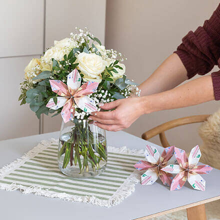 Eine gefaltete Blüte aus drei 10-Euro-Scheinen wird in einen Blumenstrauß aus weißen Rosen, Eukalyptus und Schleierkraut gesteckt