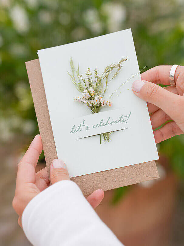 Hochzeitseinladung mit zwei Schlitzen, in die ein Mini-Trockenblumenstrauß gesteckt wurde