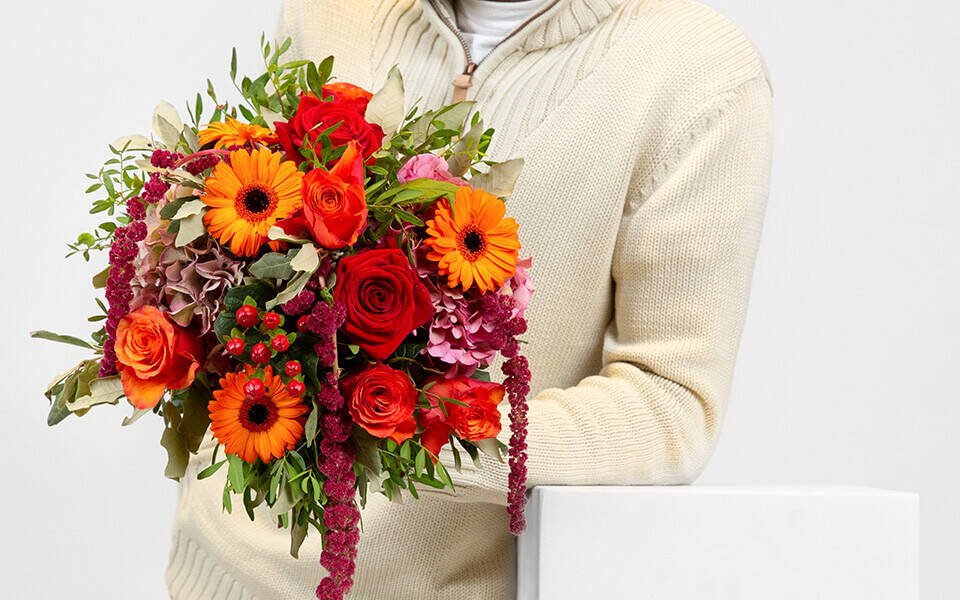 Ein mann hält einen Herbststrauß in den Farben Orange und Rot in der Hand.