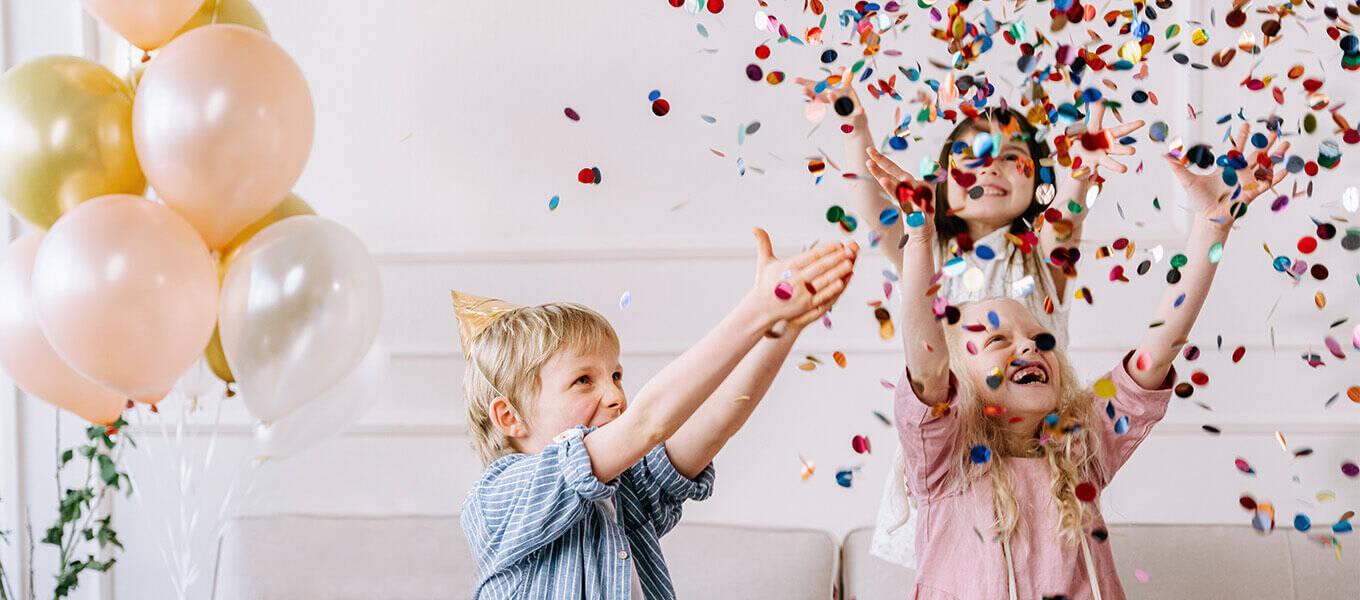 Drei Kinder, die im Wohnzimmer Konfetti auf einer Geburtstagsparty in die Luft werfen