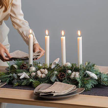 Ein länglicher Adventskranz mit vier Stabkerzen und klassischer Dekoration wie Tannenzweige, Kugeln und Baumwolle.